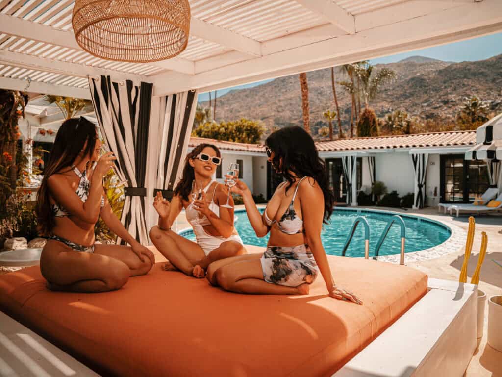 Bright women enjoying poolside drinks at a luxurious outdoor resort, relaxing under a shaded cabana with mountain views.