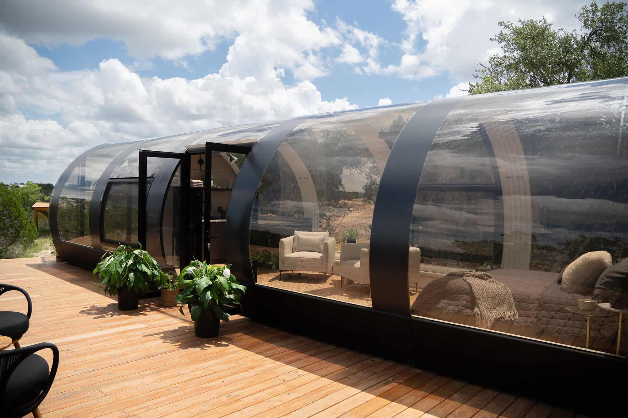 Sleek modern glamping pod with transparent bubble design on wooden deck, offering cozy outdoor living space and scenic views for outdoor enthusiasts and luxury travelers.